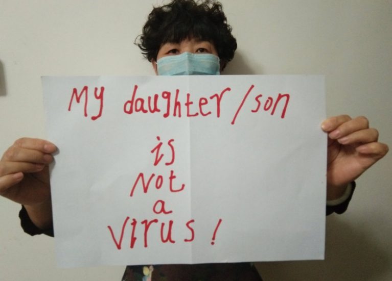Frau mit Schutzmaske hält ein Papier in die Kamera "My daughter is not a Virus"