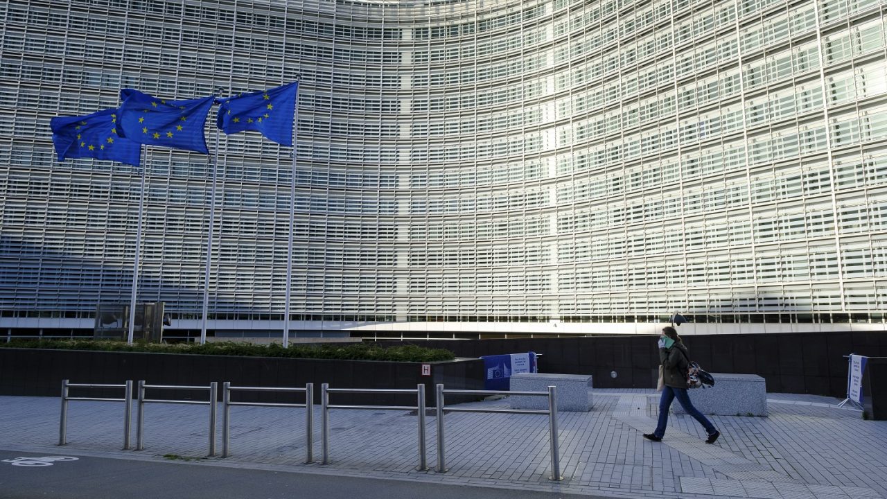 Frau mit Mundschutz läuft alleine am Gebäude der EU-Kommission vorbei