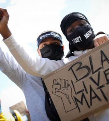Zwei schwarze Jungen stehen hintereinander und halten zusammen ein Pappschild mit der Aufschrift "Black Life Matter" vor die Brust des vorderen Jungen. Beide strecken ihre rechte Hand zu einer Faust nach oben.