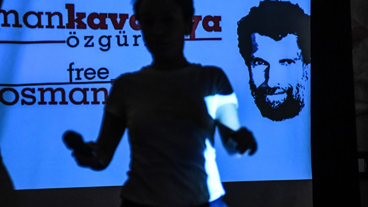 Eine Frau geht während einer Pressekonferenz an einem Bildschirm vorbei, auf dem der inhaftierte Osman Kavala zu sehen ist